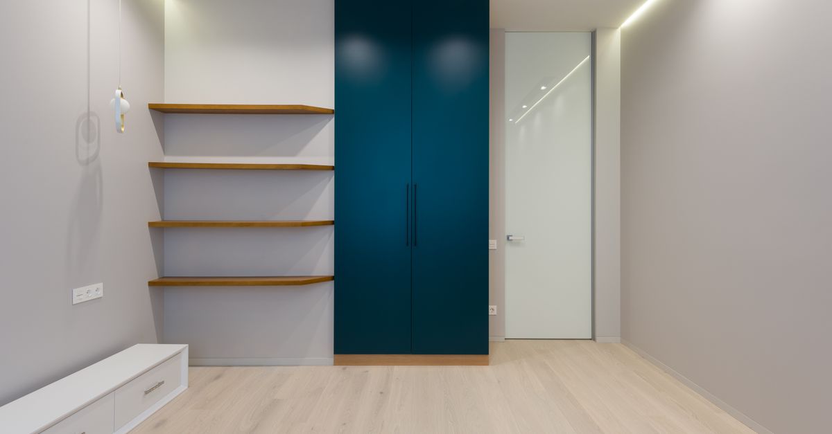 Quarto minimalista com prateleiras flutuantes de madeira na parede e um armário embutido azul-petróleo ao lado.