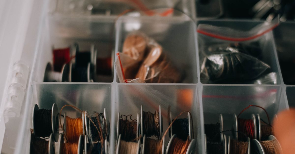 Gaveta organizada com divisórias plásticas transparentes contendo carretéis de linha e pequenos itens de costura.