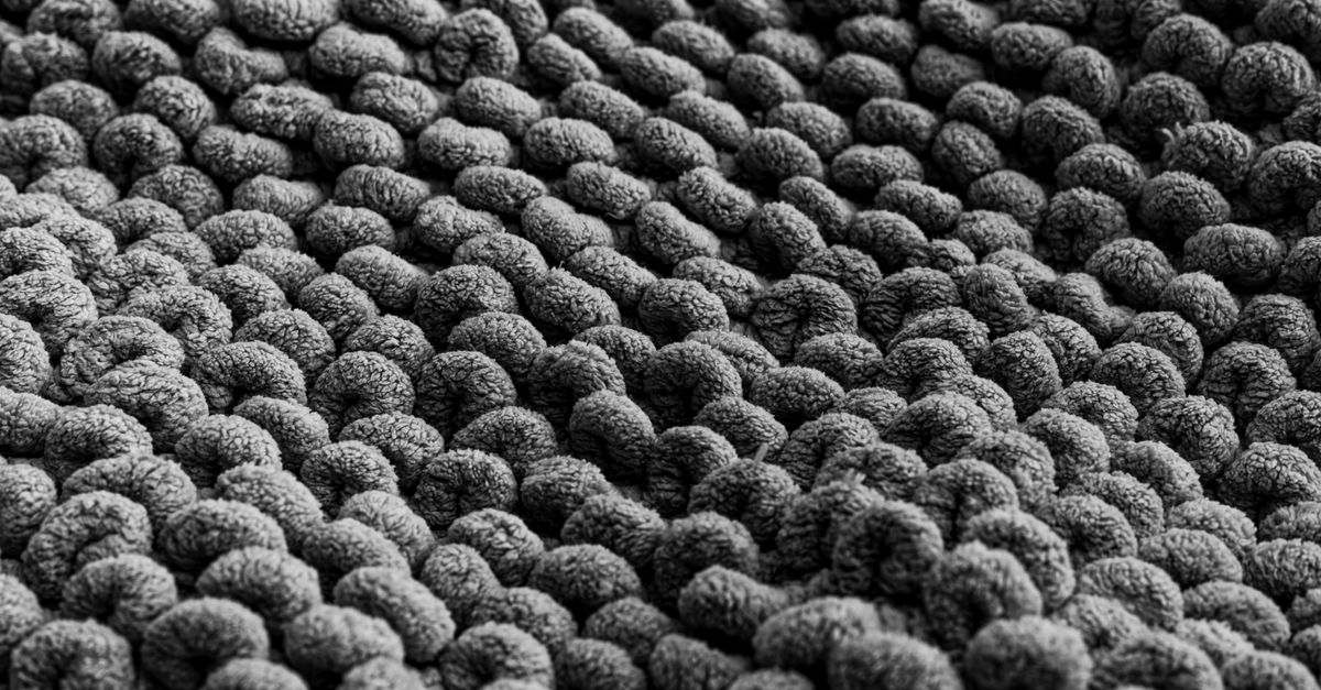 Close-up de um tapete de fibra natural em tons de cinza, mostrando a textura entrelaçada e encaracolada do tecido.