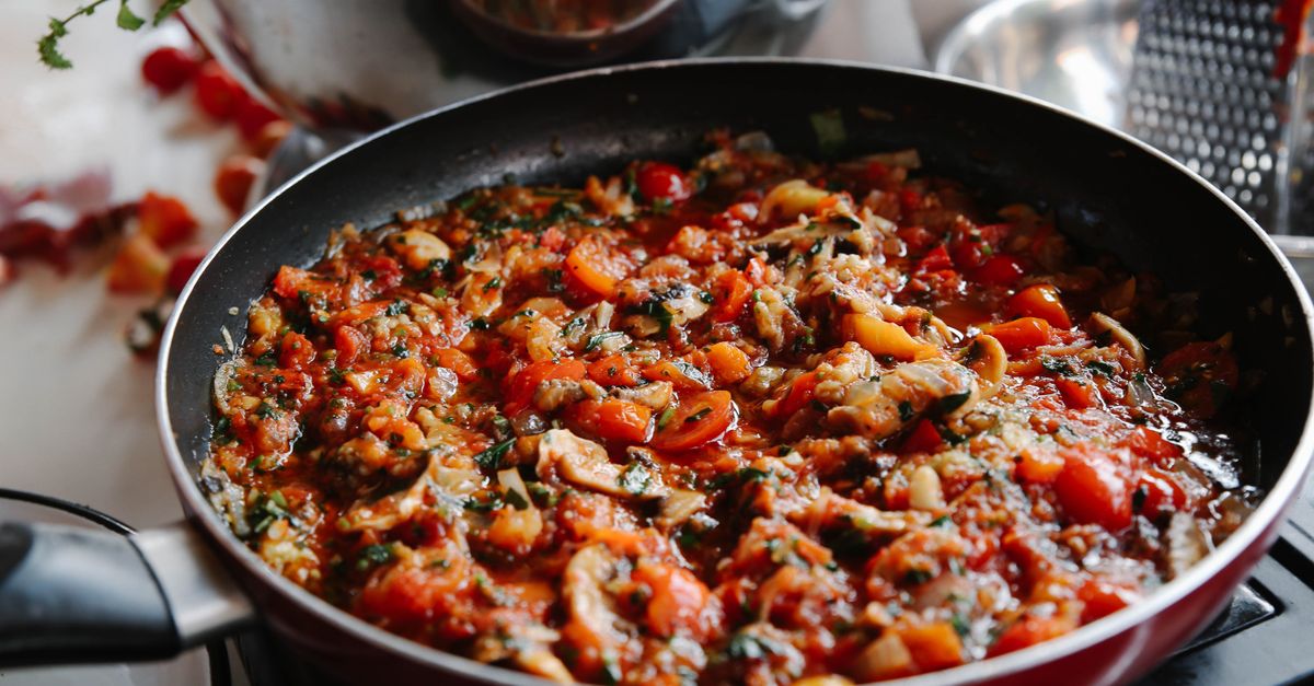 Panela com molho de tomate borbulhando no fogão, misturado com cogumelos e ervas.