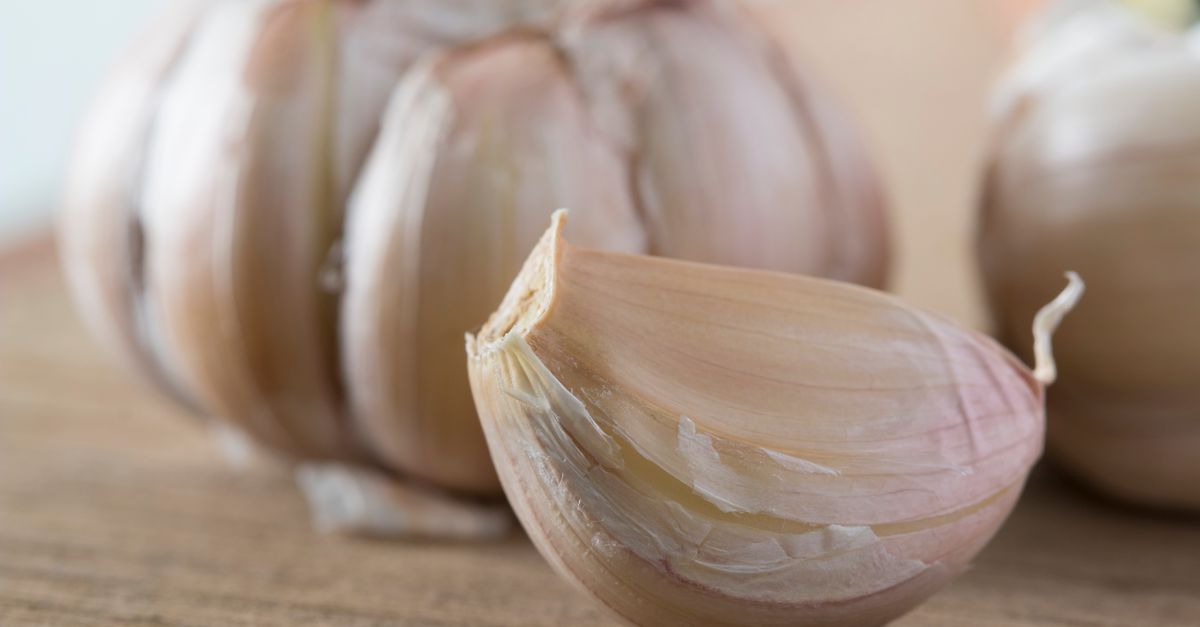 Cabeça de alho com um dente descascado em destaque sobre uma tábua de madeira
