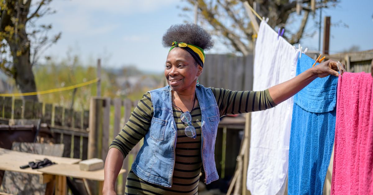 Mulher sorridente pendura toalhas coloridas em um varal ao ar livre em um dia ensolarado