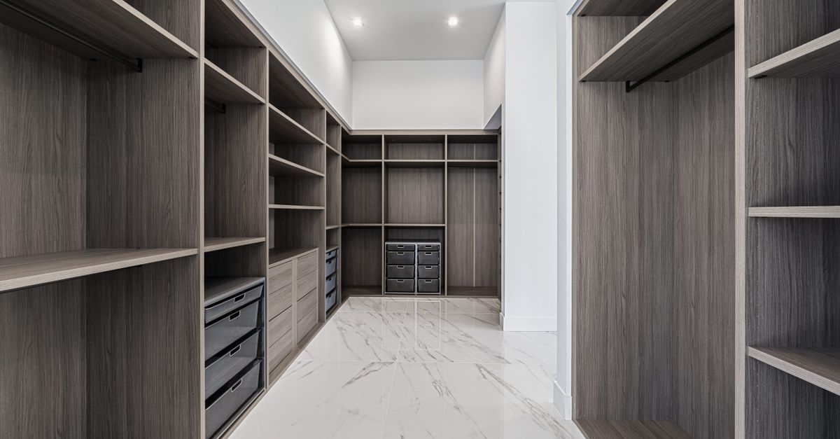 Closet organizado com prateleiras de madeira, gavetas com divisórias e cestos de tecido, piso de mármore claro.