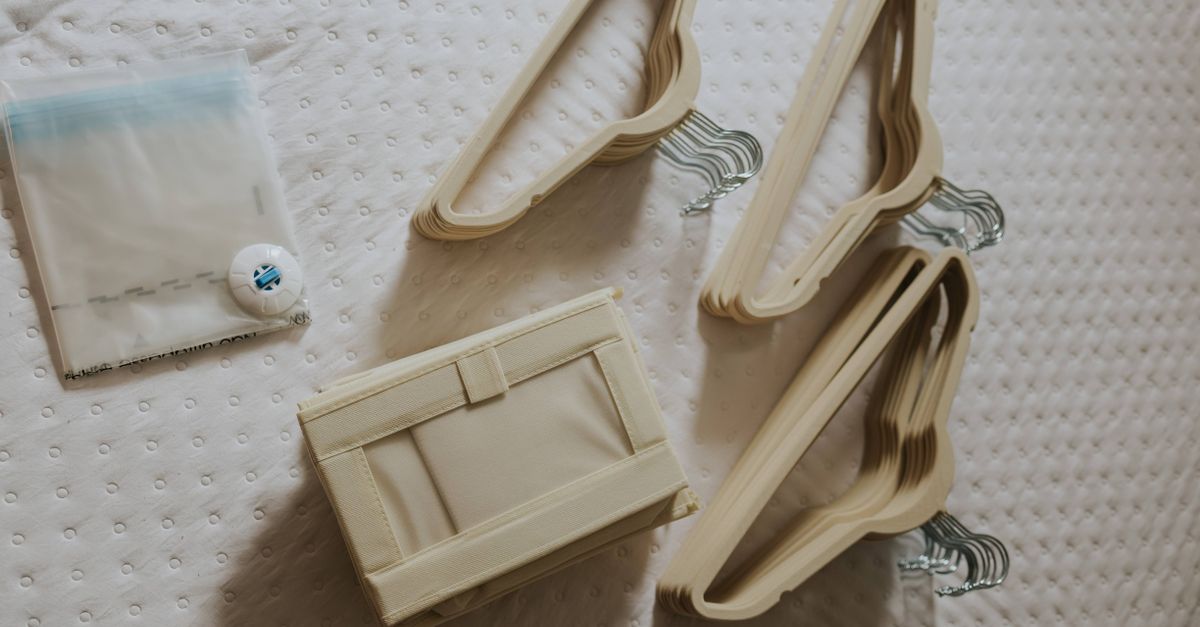 Cabides finos de plástico bege, uma caixa organizadora de tecido e um saco a vácuo dispostos sobre uma cama antes de organizar o guarda-roupa.