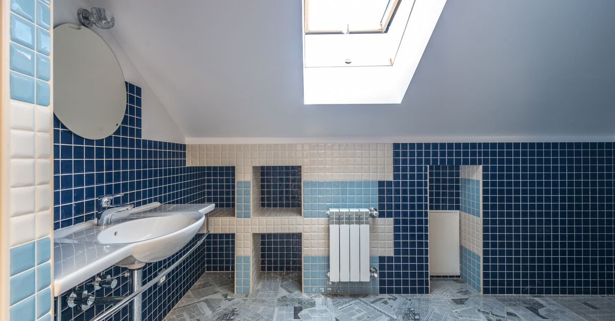 Banheiro com azulejos azuis e brancos limpos, rejunte claro entre os ladrilhos e claraboia iluminando o ambiente.