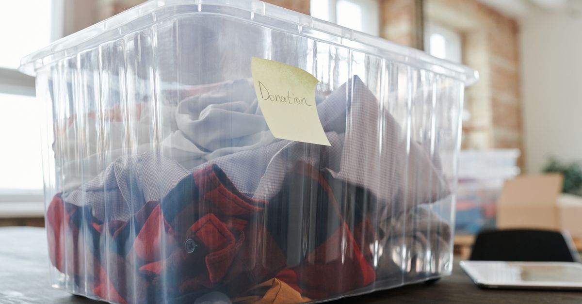 Caixa organizadora plástica transparente sobre uma mesa, contendo roupas dobradas e um bilhete adesivo com a palavra 'Donation'.