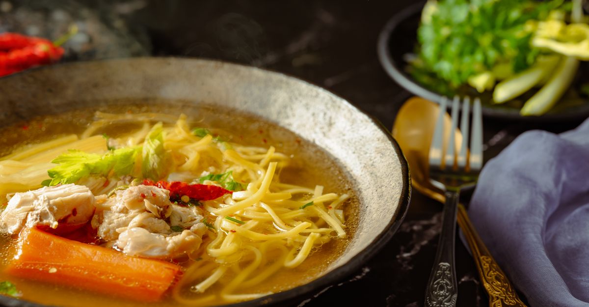 Prato de caldo caseiro com legumes como cenoura, salsão e macarrão, servido em uma tigela de cerâmica.