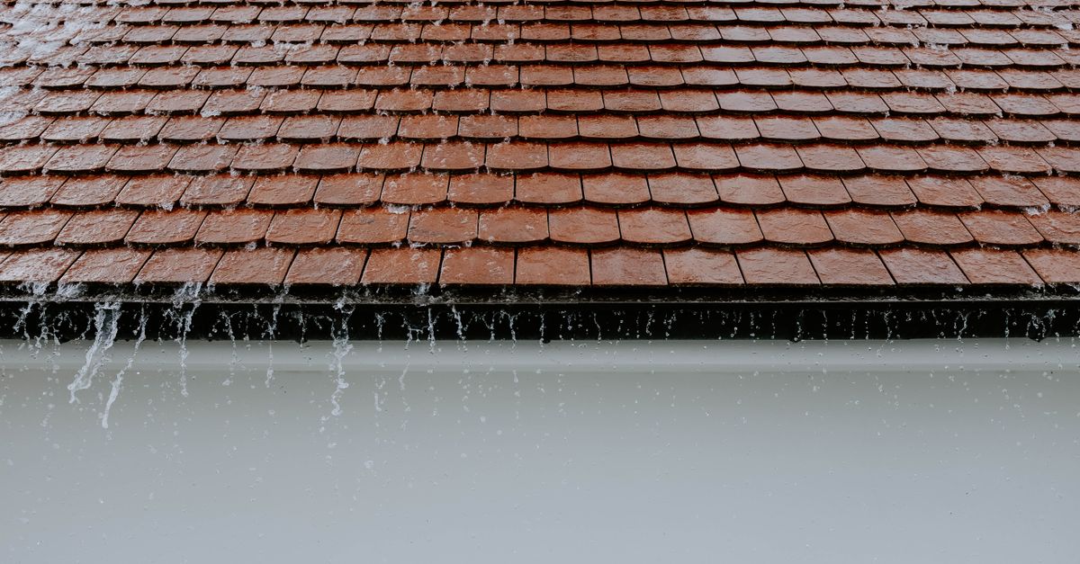Telhado de telhas cerâmicas com água da chuva escorrendo pela calha durante um temporal.