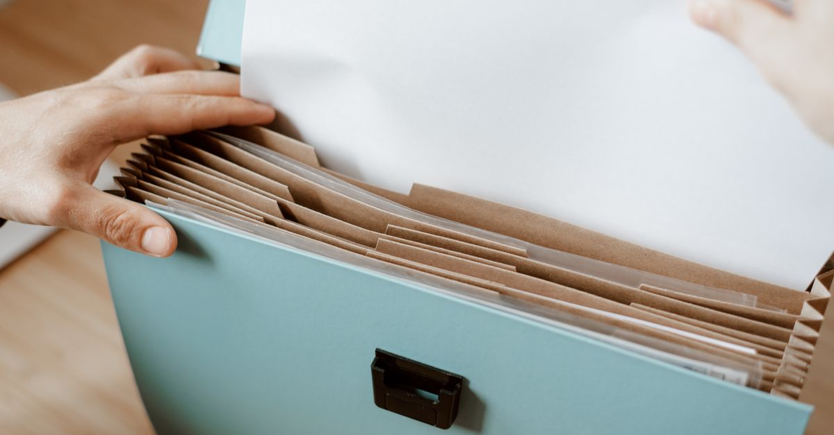 Mãos organizando documentos em uma caixa sanfonada azul com divisórias de papel kraft