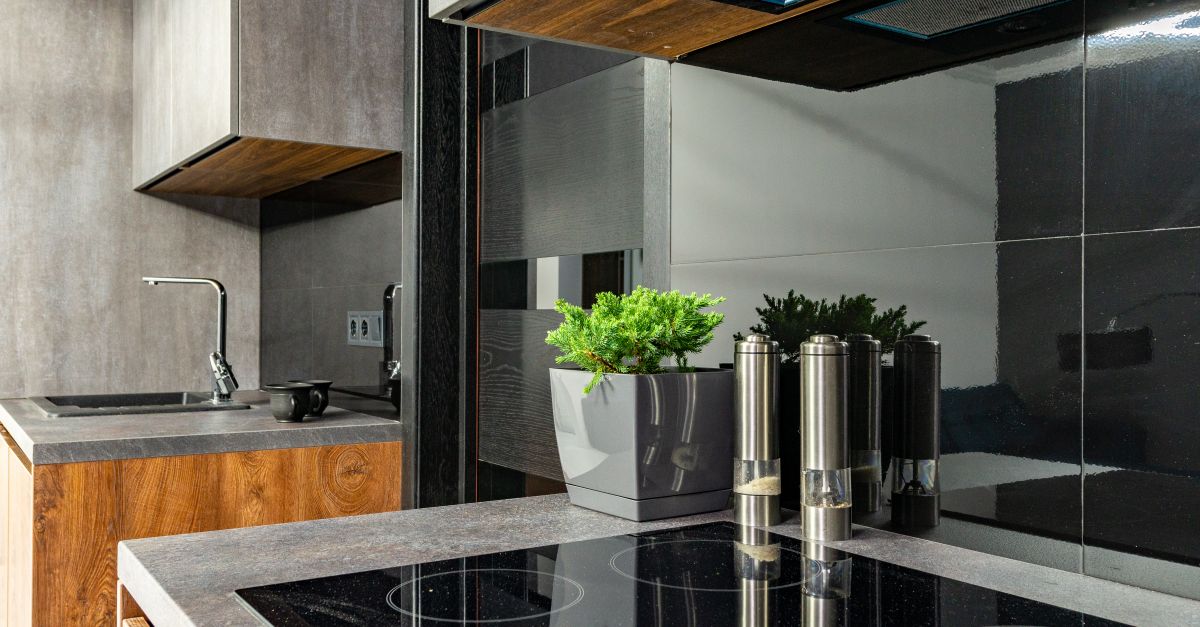 Cooktop de indução preto e brilhante em bancada de pedra escura, em cozinha moderna com planta decorativa ao fundo.