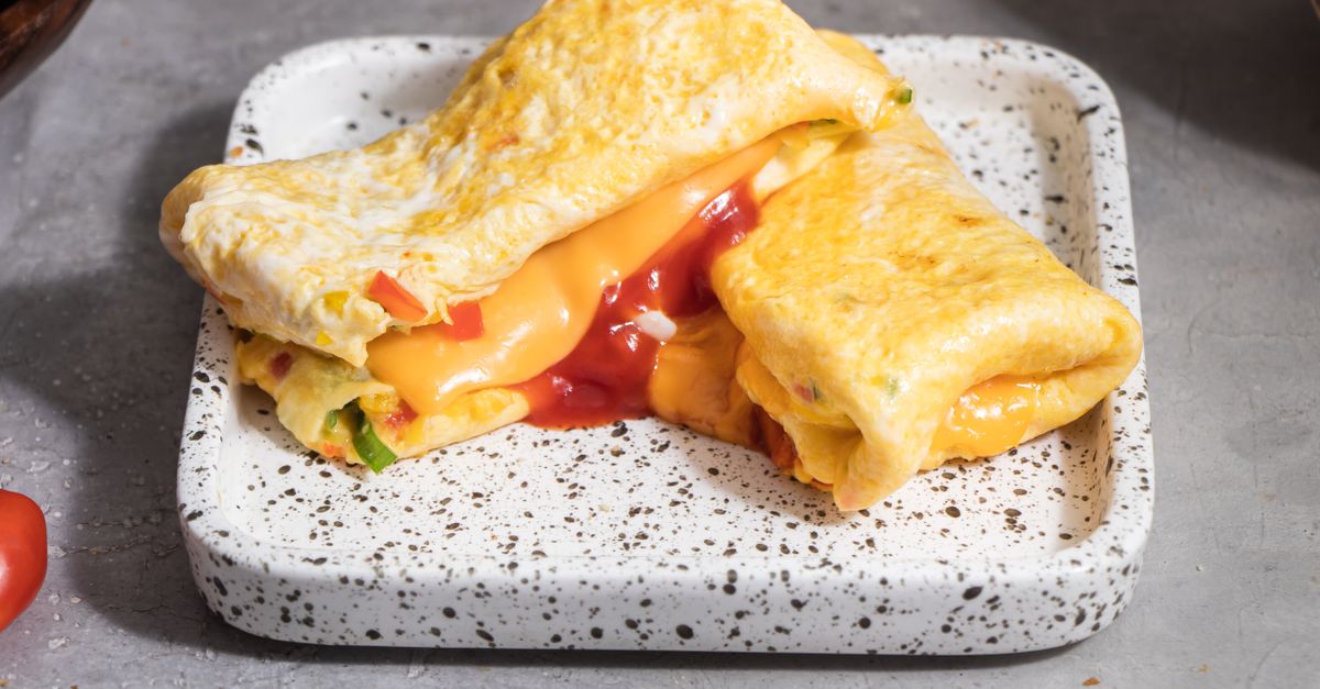 Omelete dobrada recheada com queijo derretido e pimentões, servida em prato branco speckled com um fio de ketchup.