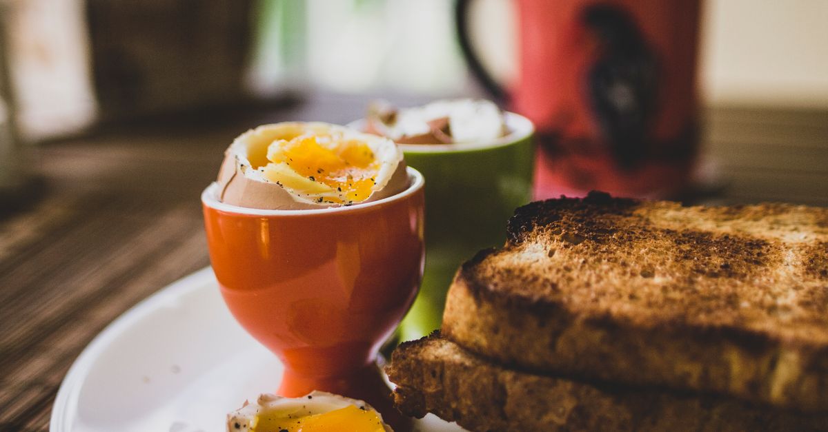 Ovos cozidos moles servidos em suportes coloridos, com a gema líquida aparecendo, ao lado de torradas tostadas.