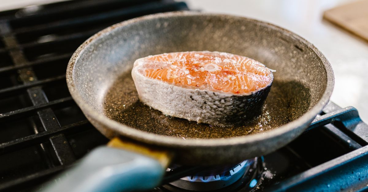 Posta de salmão sendo selada e dourada em frigideira com óleo quente sobre fogão